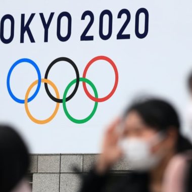 Tokyo 2020 logo with people with facemaks in foreground