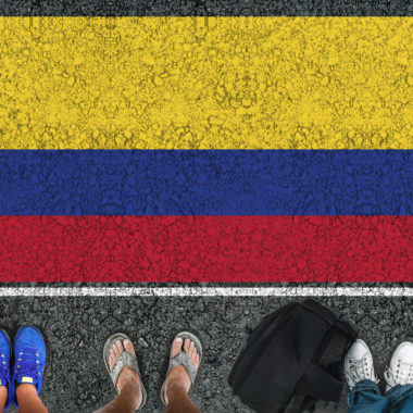 Legs standing on road next to flag of Colombia and border.