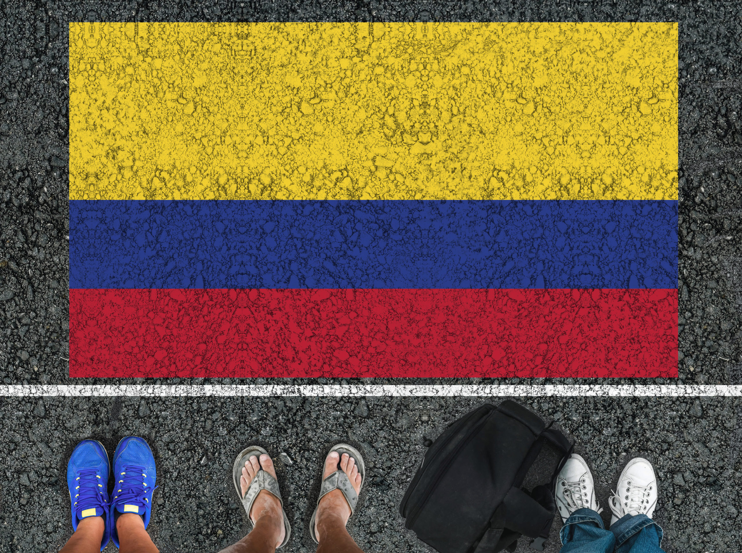 Legs standing on road next to flag of Colombia and border.